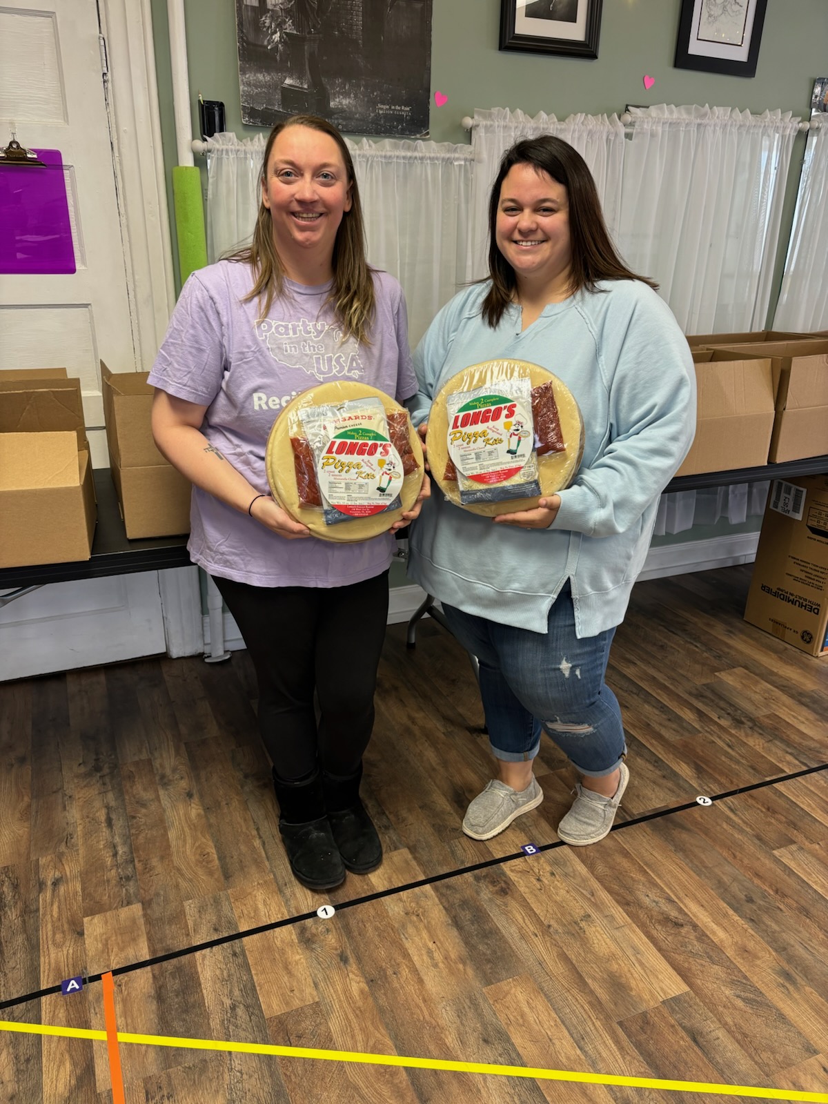 Two women posing with ATV Bakery boxes in a classroom for Tasty Choices Fundraising